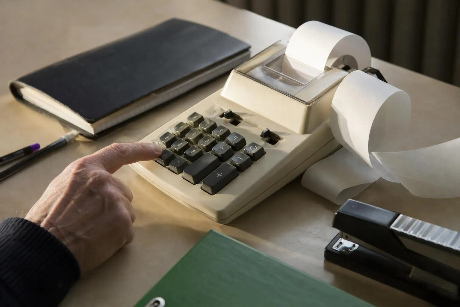 Une calculatrice de bureau à bande papier posée sur un plan de travail, avec le ruban imprimé qui se déroule sur le côté.