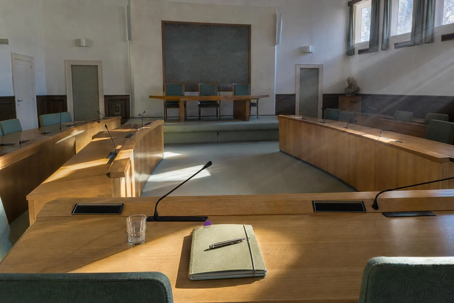 Une salle du conseil municipal vide en début de matinée, avec une chemise cartonnée posée sur un pupitre en bois.