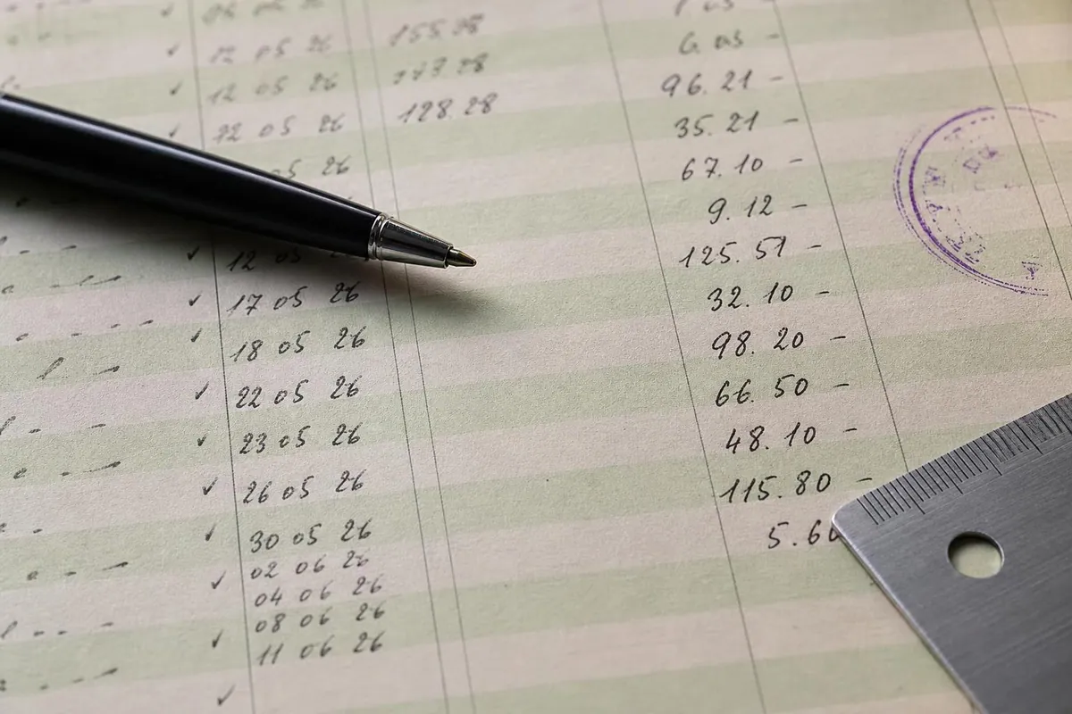 Gros plan sur une page de registre comptable à colonnes vertes portant des montants manuscrits alignés et un tampon d'encre violette dans la marge